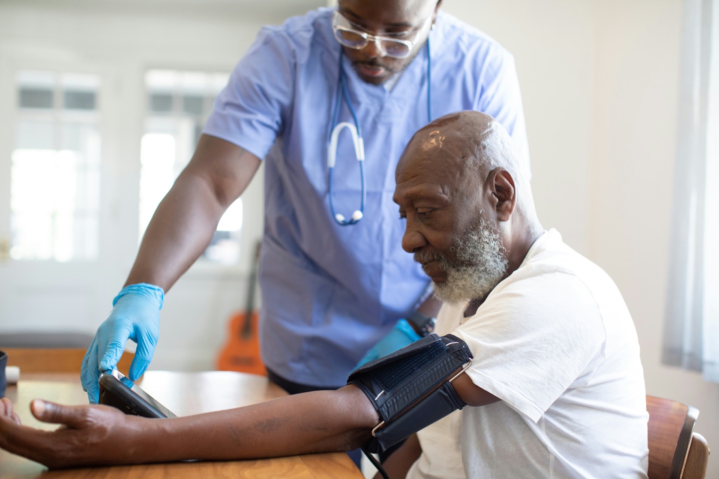 Healthcare professional in blue scrubs checking an older adult’s blood pressure